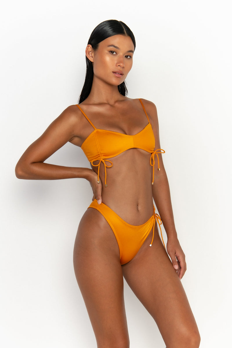 side view elegant woman wearing luxury swimsuit from sommer swim - bea turmeric is a light orange bikini with bralette bikini top
