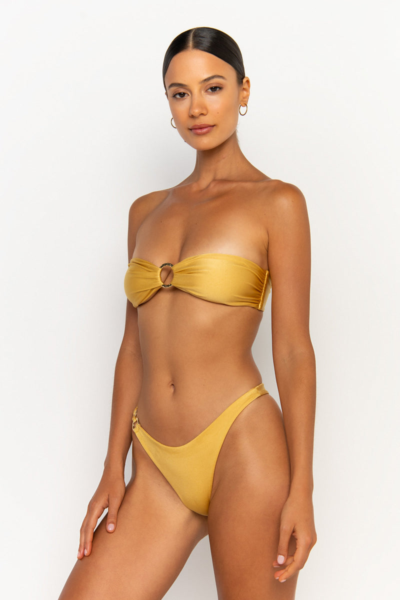 side looking front view elegant woman wearing luxury swimsuit from sommer swim - cece lusso is a golden bikini with a bandeau bikini top