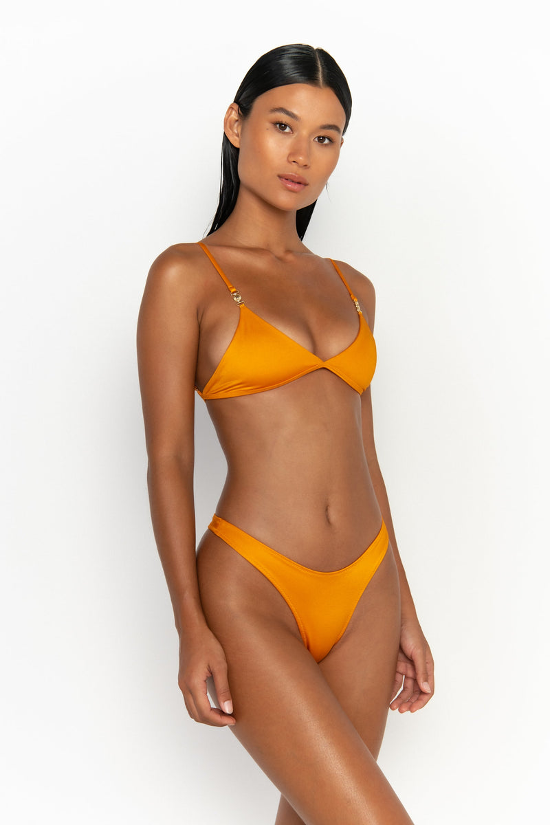 side view elegant woman wearing luxury swimsuit from sommer swim - niam turmeric is a light orange bikini with thong bikini bottom