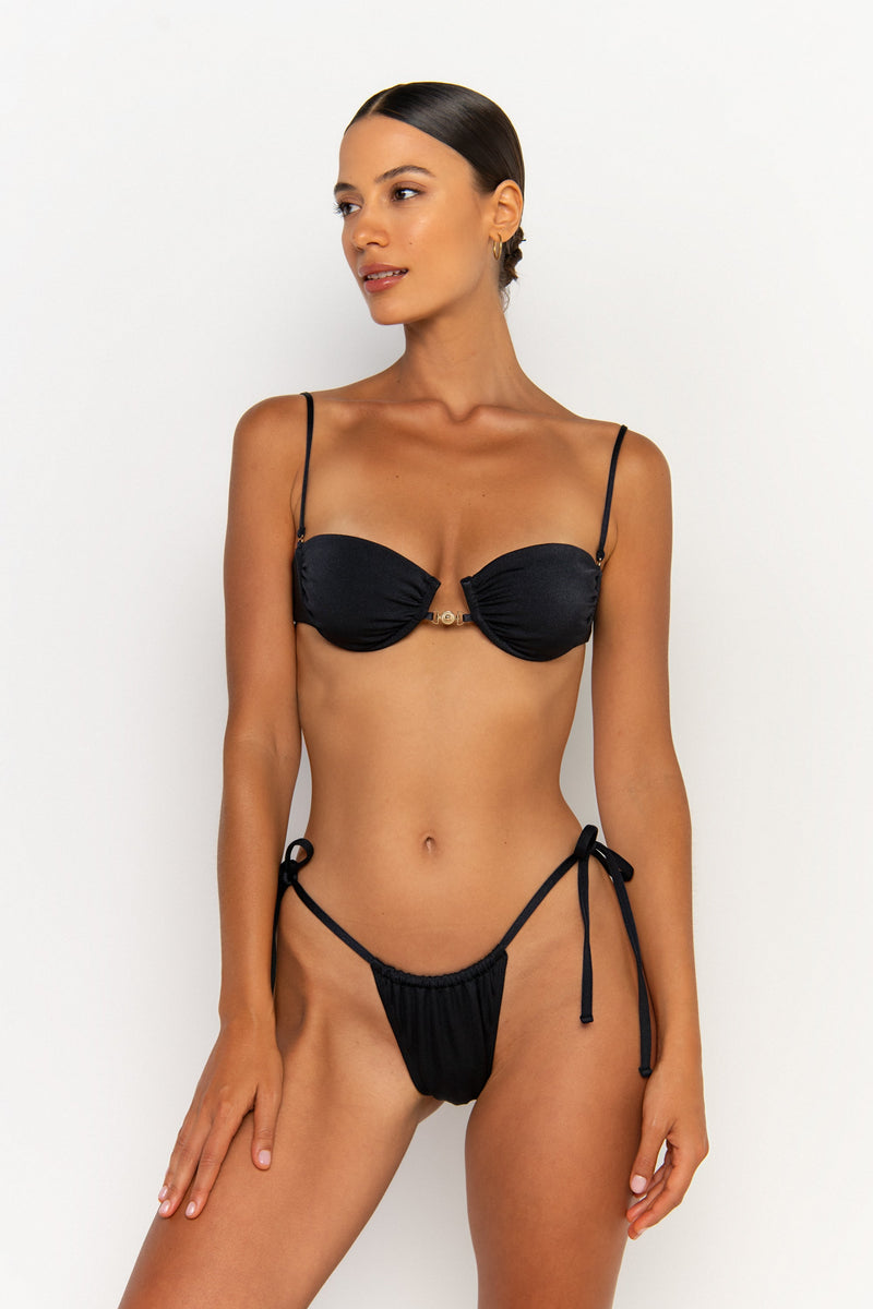 front looking sideways view elegant woman wearing luxury swimsuit from sommer swim - paloma nero is a black bikini with tie side bikini bottom
